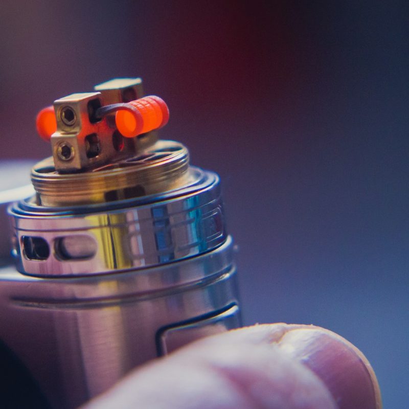 cigarette électronique posée sur un doigt avec bobine orange et réservoir métallisé