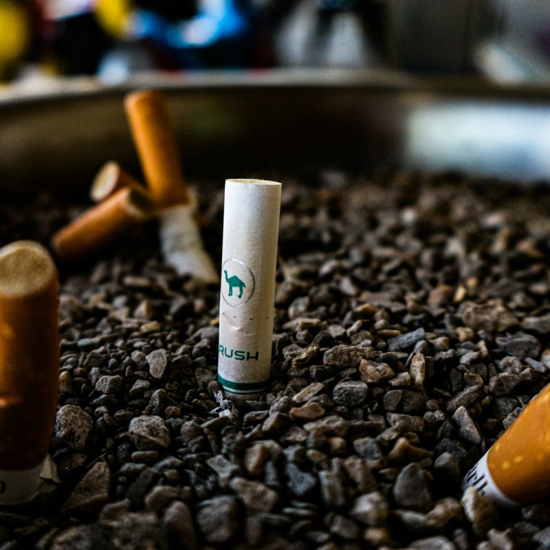 cigarettes écrasées sur des cailloux, dont une marquée "RUSH" au centre