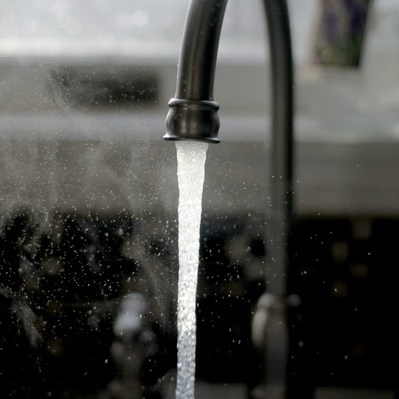 robinet ouvert avec jet d'eau visible, symbolisant la consommation d'eau