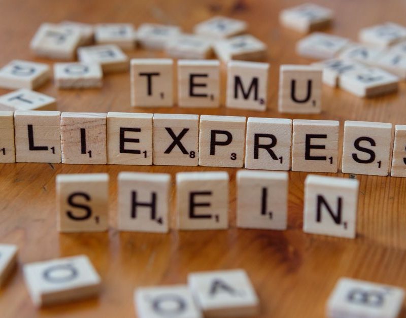 Wooden Scrabble tiles display popular e-commerce platforms on a wooden surface.