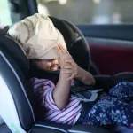 A child has a bag over their head in car.
